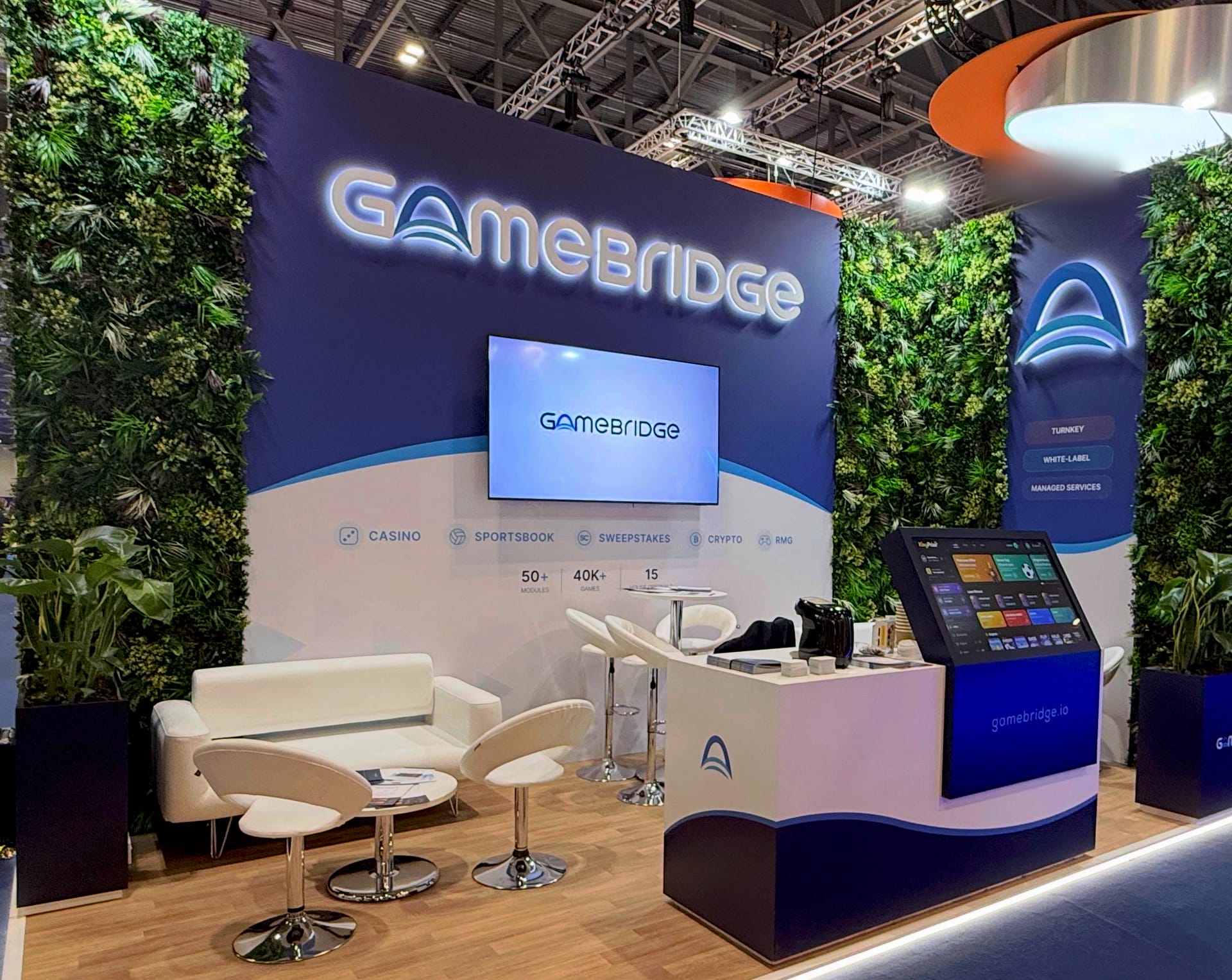 Wide view of the GameBridge stand at iGB L!VE London 2026 with its green walls, lounge seating and demo console